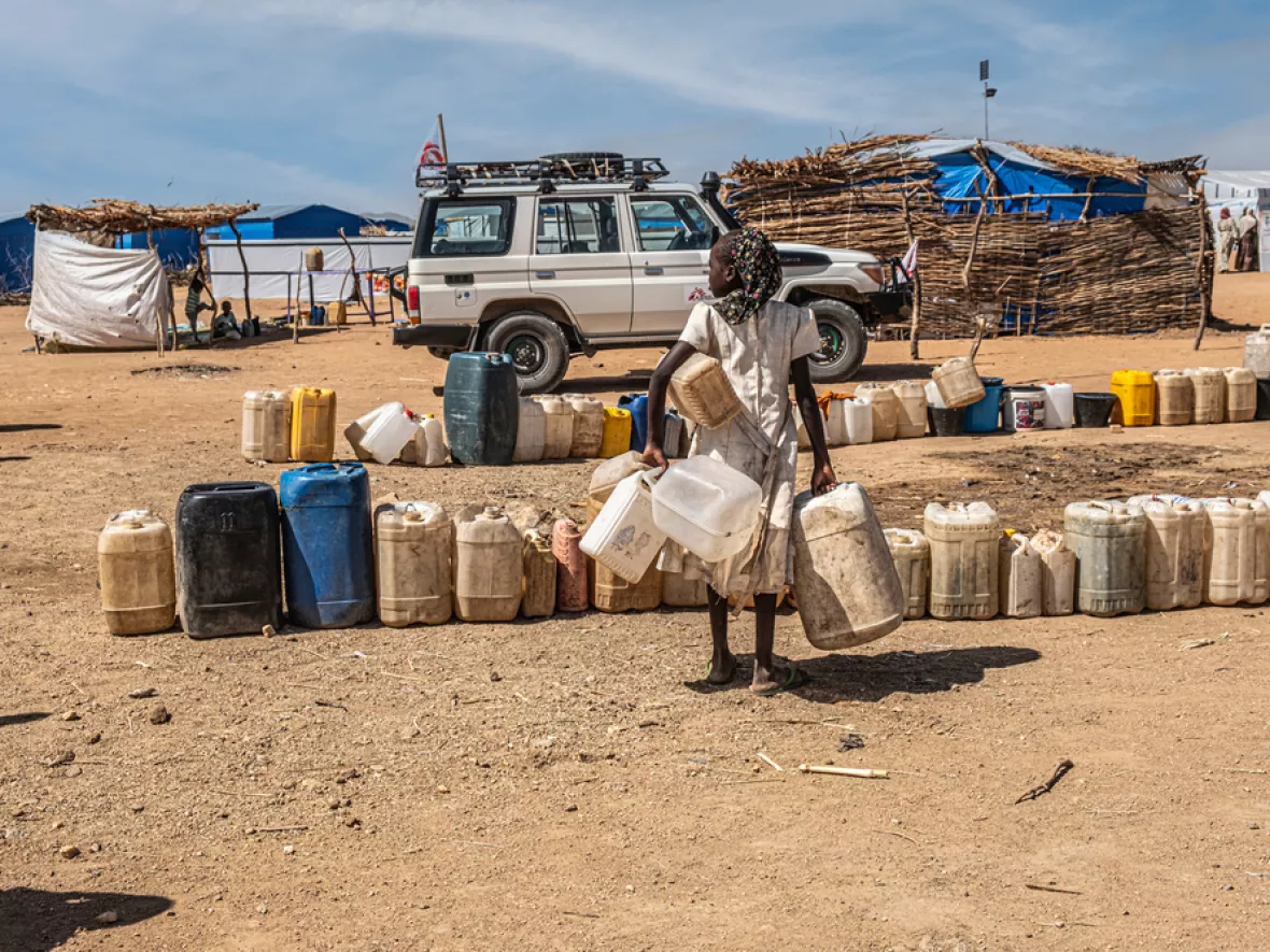 Person vor Wasserbehältern in Sandlandschaft