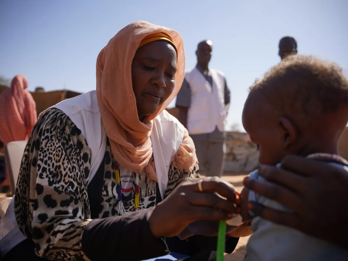 Sudan: Mitarbeiterin prüft auf Mangelernährung an Arm von Kleinkind  