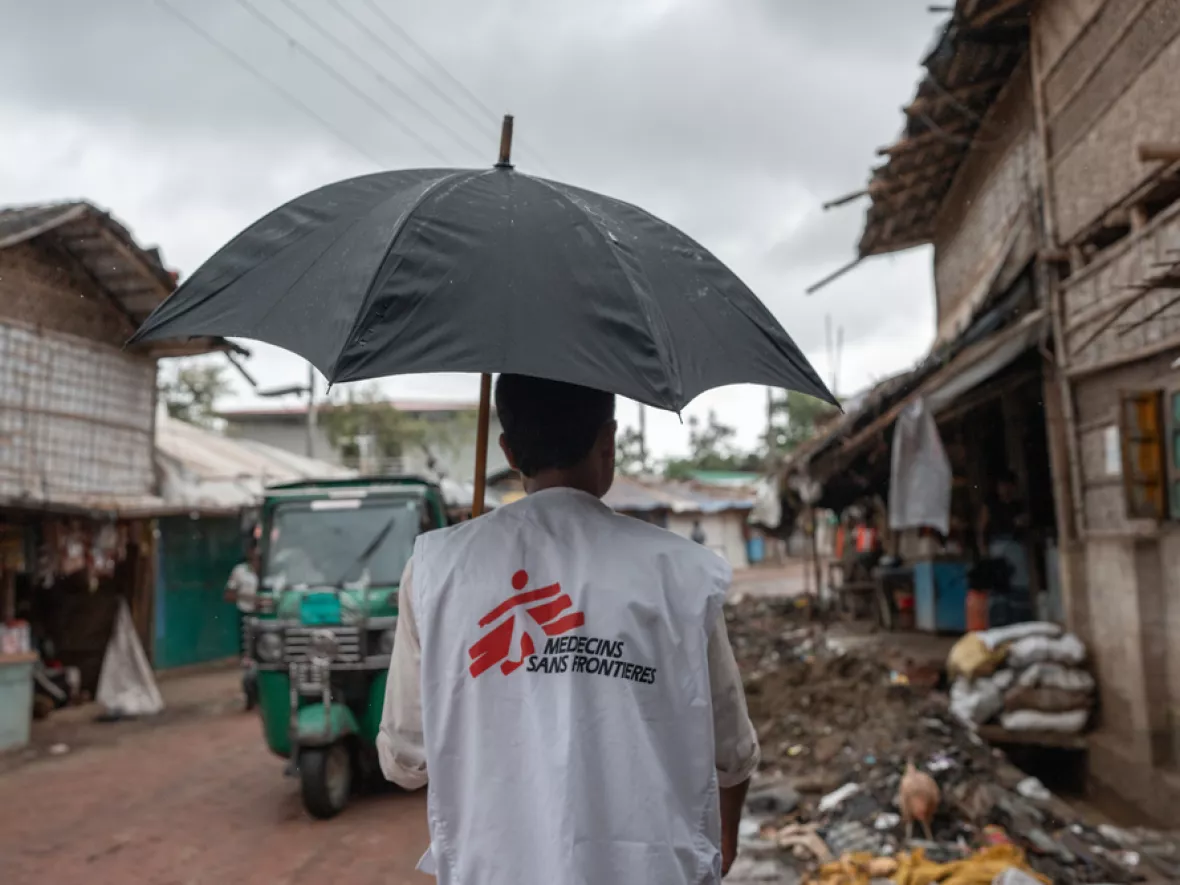 Ein Mitarbeiter von Ärzte ohne Grenzen läuft unter einem Regenschirm durch das Camp.