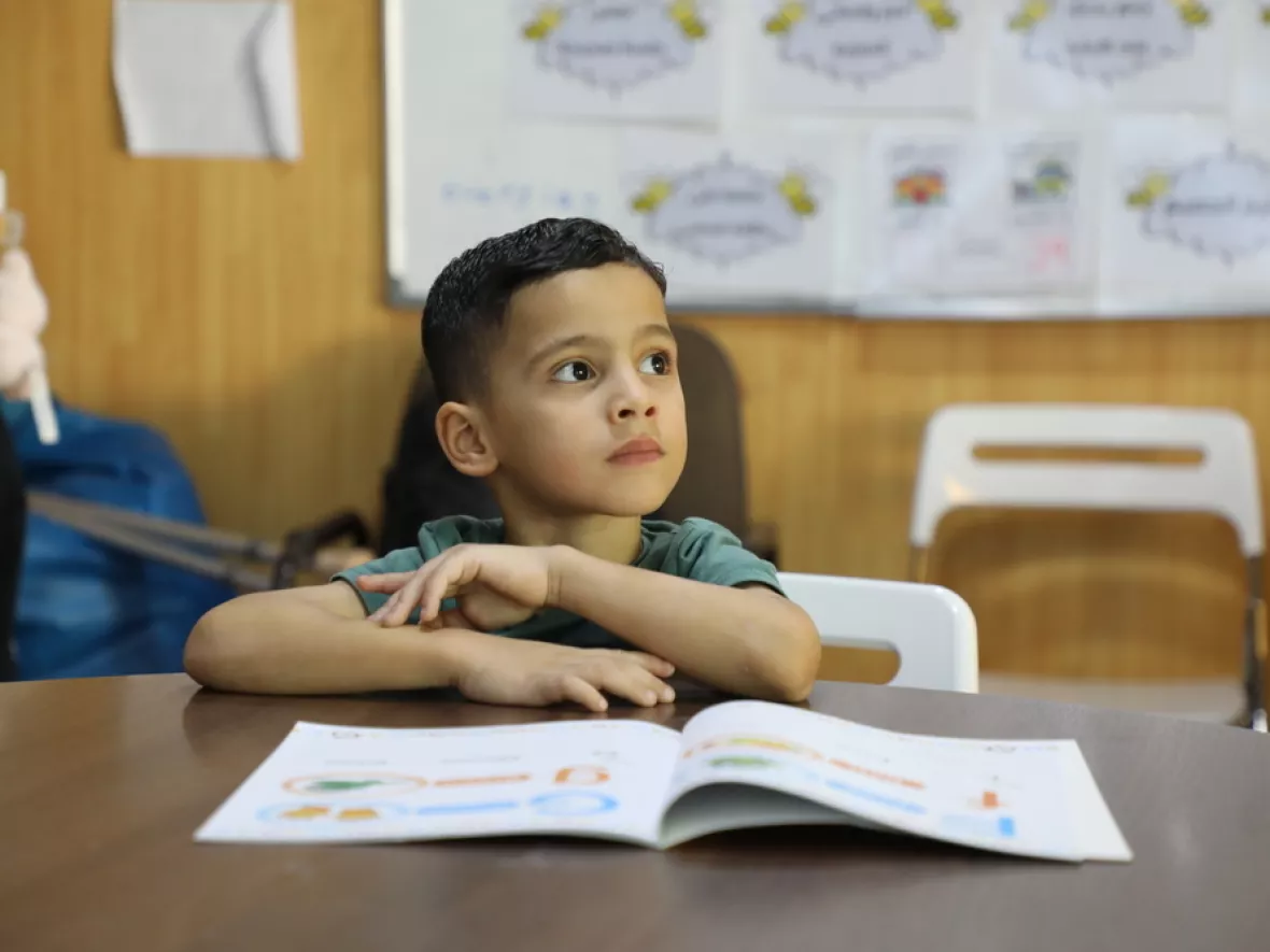 Omar sitzt am Tisch und hat ein Schulheft vor sich liegen.