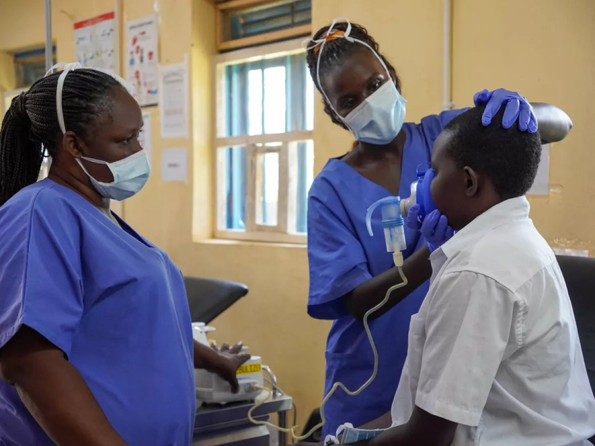 Pflegerin setzt Patienten Inhalator auf, während Kollegin zusieht