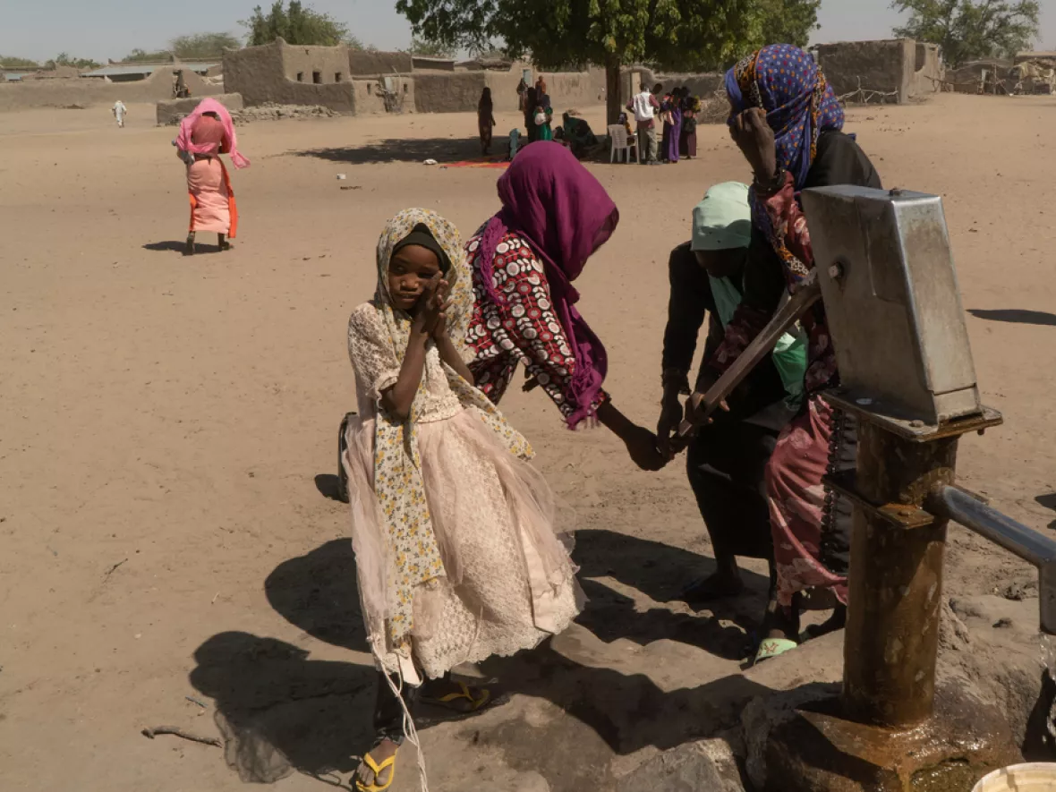 Vier Frauen stehen um eine Wasserquelle.