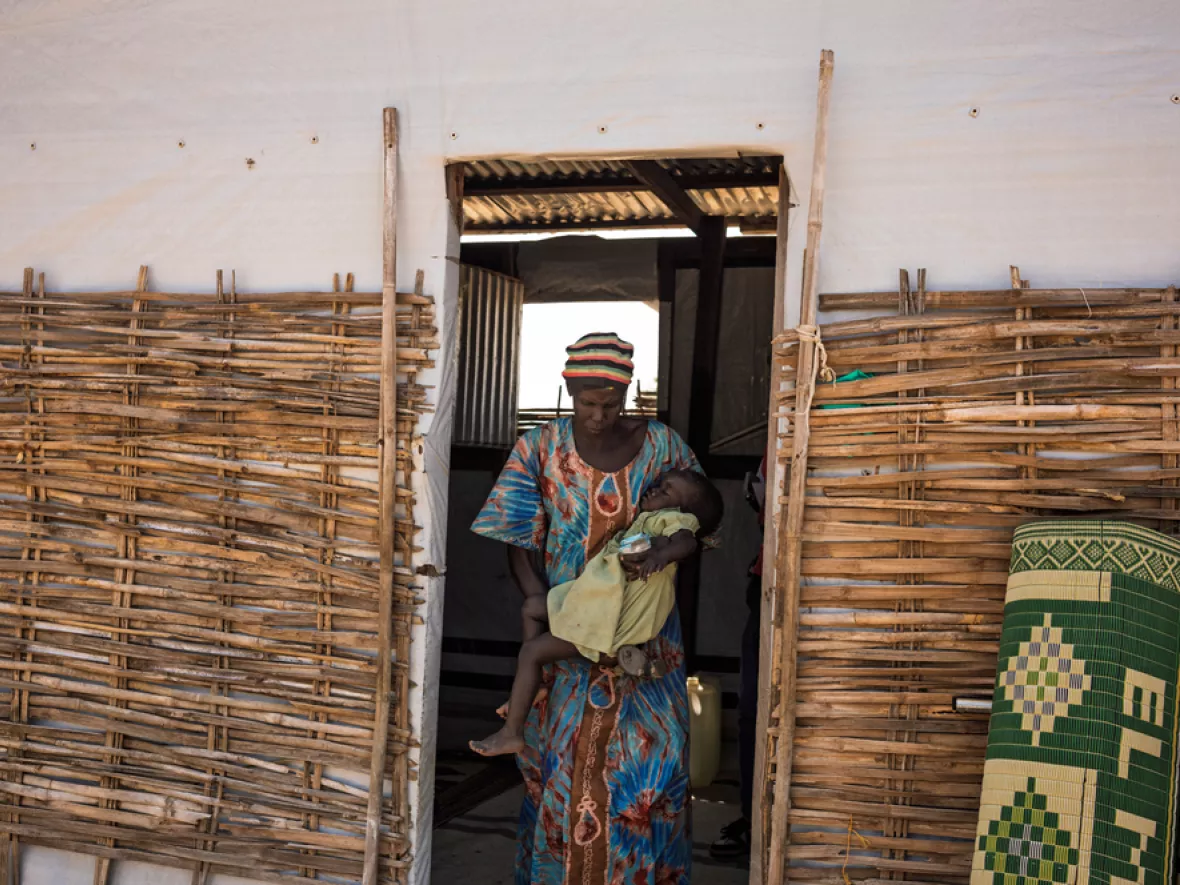 Frau mit Kleinkind im Arm kommt aus Tür
