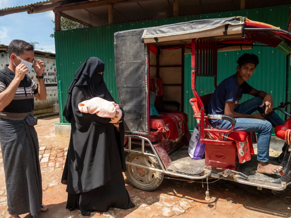 Ein Mann und eine Frau stehen neben einem Tuk-Tuk in dem noch ein Mann sitzt