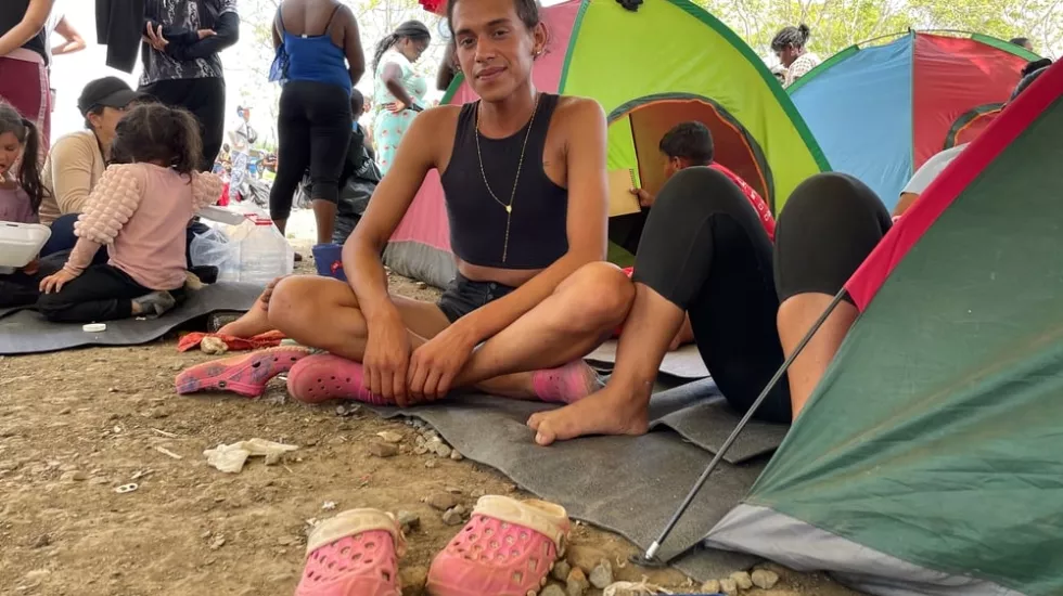 Eine trans*Frau im Schneidersitz vor einem Zelt.