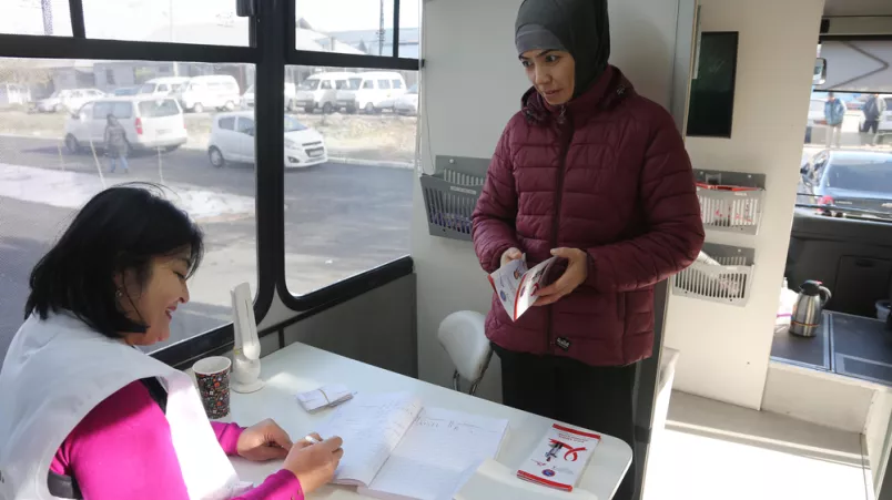 Eine Ärztin sitzt am Tisch und schreibt, eine Patientin steht davor