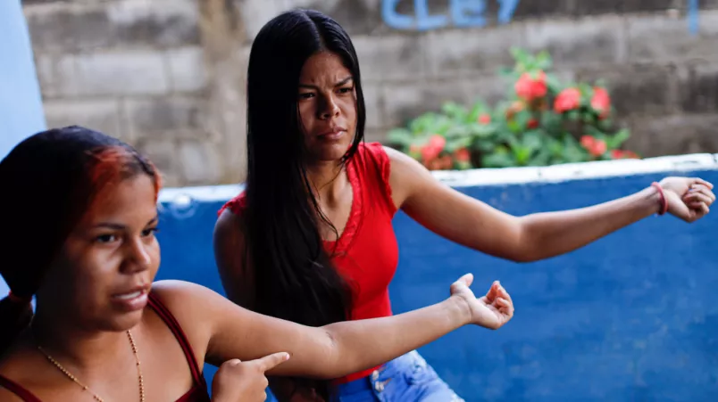 Zwei Frauen deuten jeweils auf ihren linken ausgestreckten Oberarm