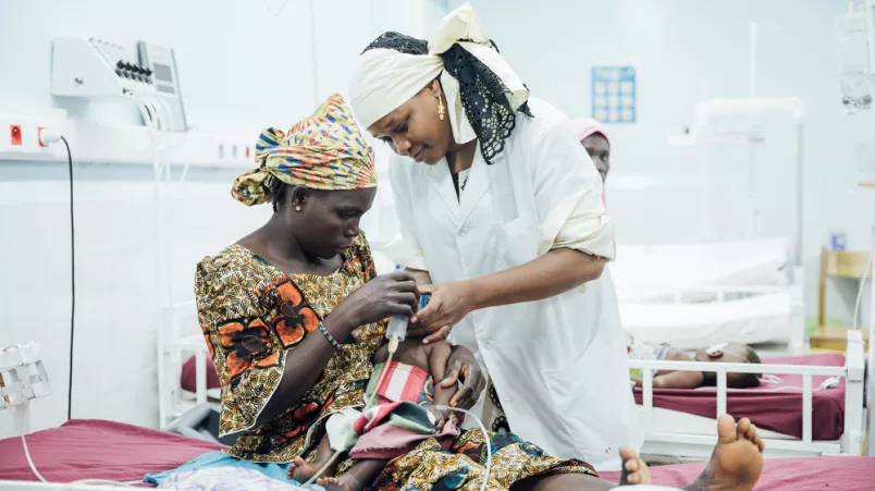 Krankenpflegerin versorgt Baby in Armen der Mutter