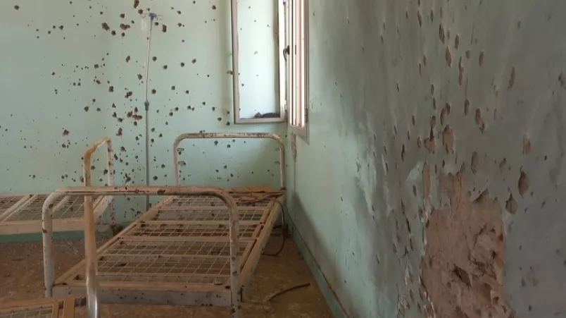 Verrostete Krankenbetten stehen in einem Raum mit Einschusslöchern.