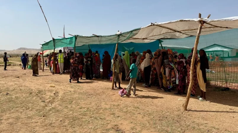 Gruppe an Frauen steht in einer Schlange unter einem Vorzelt.