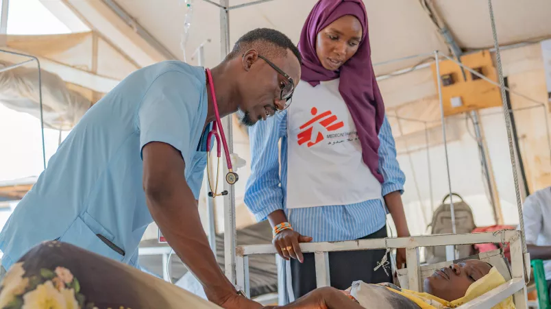 Gesundheitsberaterin Aisha B. übersetzt zwischen Arzt und Patientin. Zwei Mitarbeitende behandeln eine Patientin.