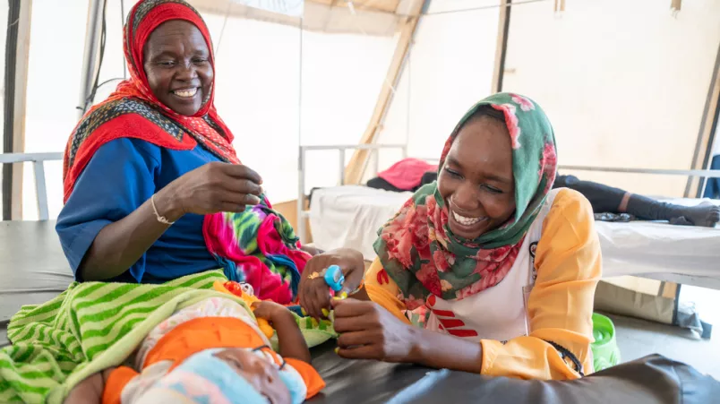 Zwei Mitarbeiter kümmern sich um ein kleines Kind, während seine Mutter von unserem Team behandelt wird.  Zwei Mitarbeiterinnen kümmern sich um ein Kleinkind.