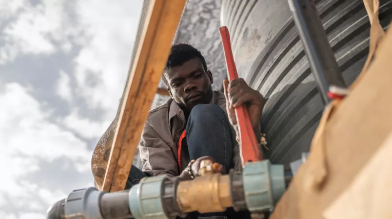 Ein Mitarbeitender repariert einen Wassertank, im Transitcamp Adré, im Tschad.  Mitarbeitender repariert einen Wassertank.