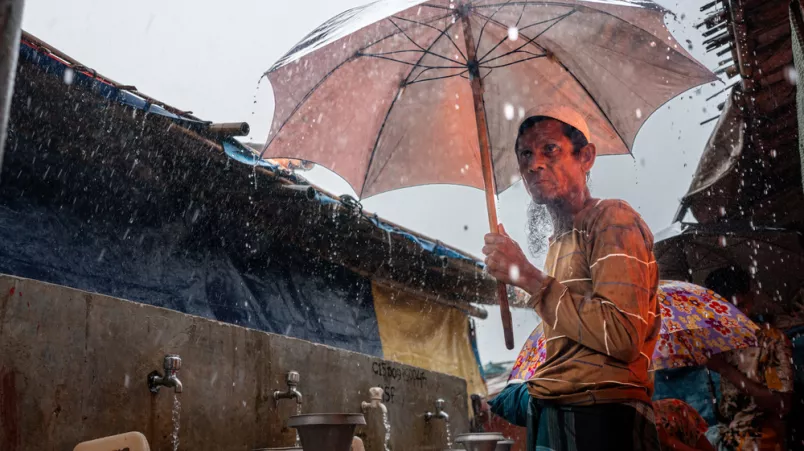 Ein Mann steht unter einem großen Regenschirm an einer Wasserstelle im Camp..