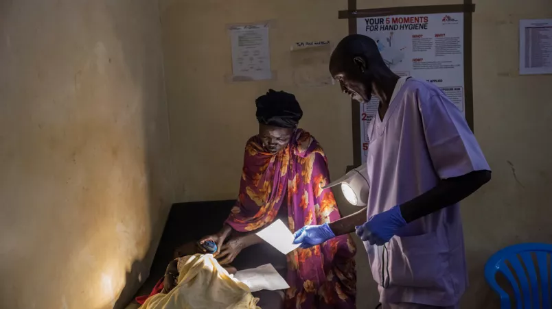 Mitarbeiter und Mutter stehen an Behandlungsbett mit Kind, darauf
