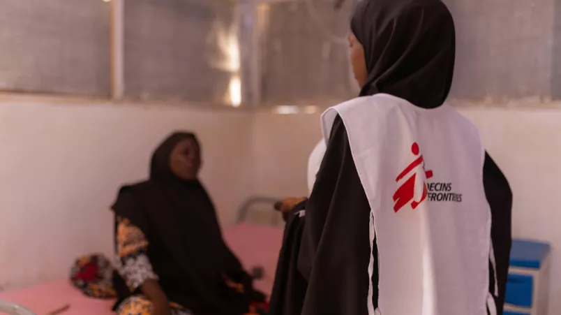 Patientin auf Behandlungsliege spricht mit stehender Mitarbeiterin