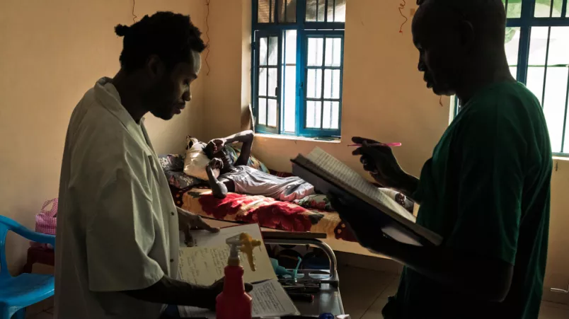 Zwei Mitarbeitende vor Patientenbett schauen in Unterlagen