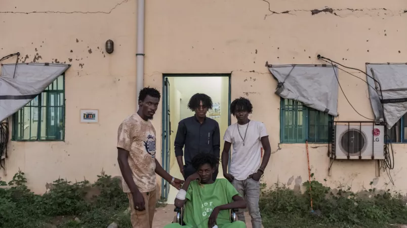 Junger Mann in Rollstuhl, drei Männer stehen hinter ihm