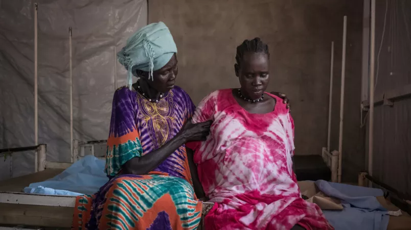 Schwangere neben ihrer Mutter auf Krankenbett sitzend