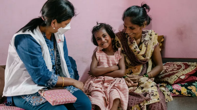 Eine unserer Mitarbeiterinnen spricht mit einem Kind und seiner Mutter. Alle lachen.