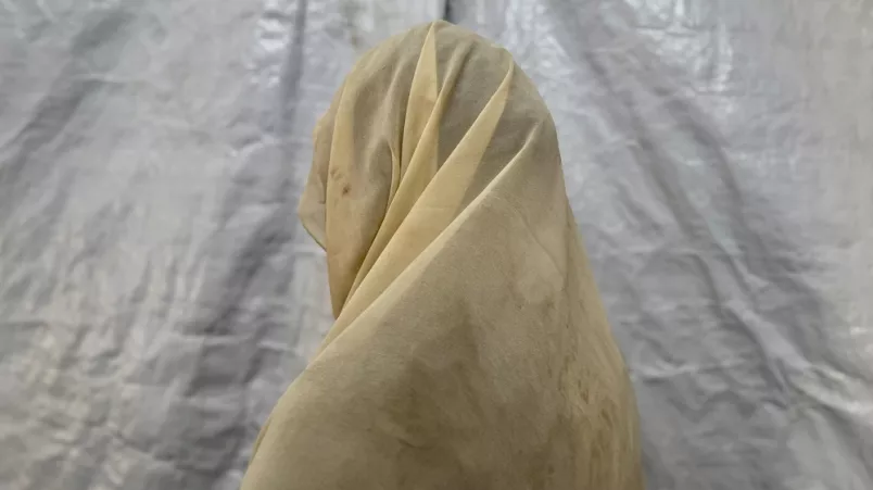 Eine junge Frau mit hellem Tuch über dem Kopf steht in einem Zelt in einem Vertriebenencamp in Sudan.