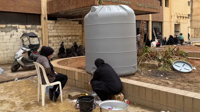 2 Frauen spülen Geschirr an einem Wassertank.