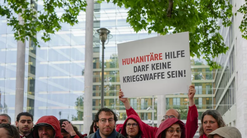 Menschen demonstrieren: "Humanitäre Hilfe darf keine Kriegswaffe sein!" steht auf einem Schild