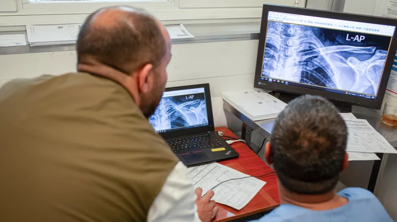 Zwei medizinische Mitarbeiter betrachten die Röntgenaufnahme einer Schulter.