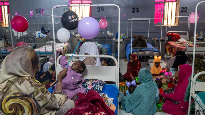 Mütter und Kinder sind auf einer Station. Es hängen Luftballons und sie spielen miteinander.