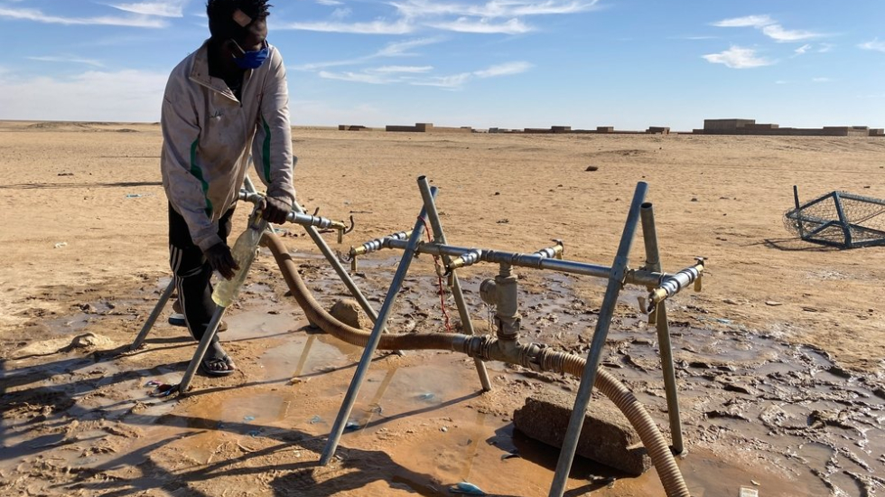 Ein junger Mann füllt sich an einer Wasserpumpe in der Wüste ab