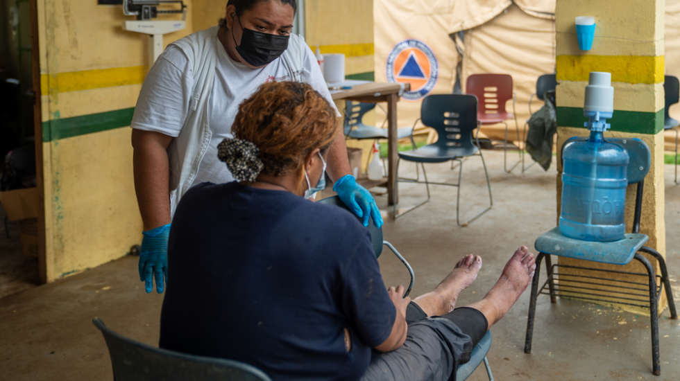 Eine Pflegerin von Ärzte ohne Grenzen kümmert sich um eine Frau, die ihre Füße auf einen Hocker gelegt hat.