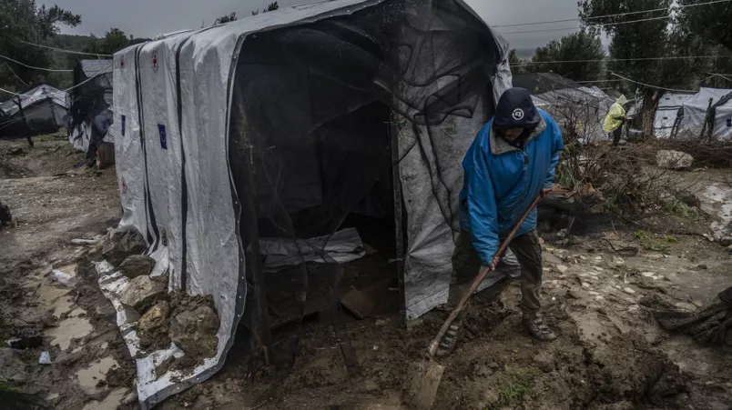Ein Mann schaufelt vor einem Zelt Matsch mit einer Schaufel