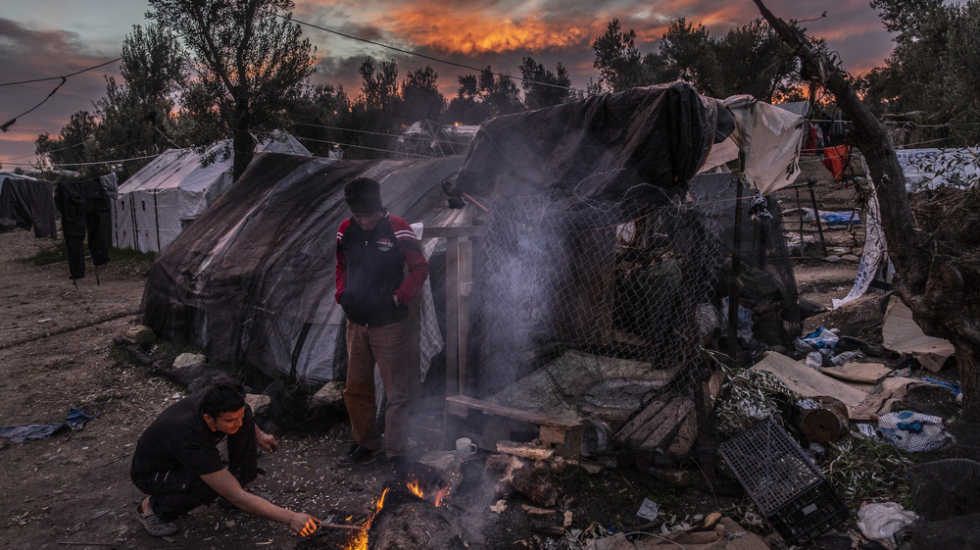 Eine Landschaft mit vielen schmutzigen Zelten, vor einem kauern zwei Menschen und machen ein Feuer