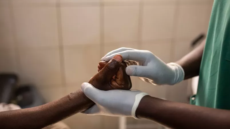 Zwei Hände mit medizinischen Handschuhen halten eine andere Hand 