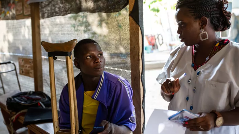 Mann mit Krücke sitzt, neben ihm Psychologin 