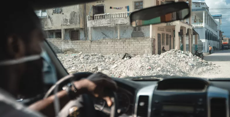 One of our employees is sitting in a car. In the background, there is visible destruction due to an earthquake.