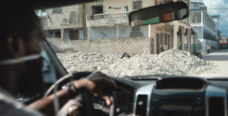 One of our employees is sitting in a car. In the background, there is visible destruction due to an earthquake.