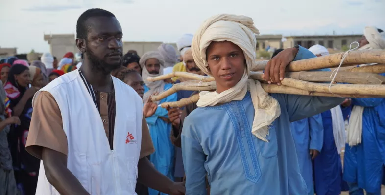 Ein junger Mann mit Material für eine Notunterkunft und ein Mitarbeiter von Ärzte ohne Grenzen in Mali.
