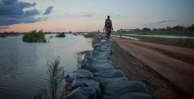 Frau läuft im Südsudan einen Deich enlang - Flutwasser ist überall.