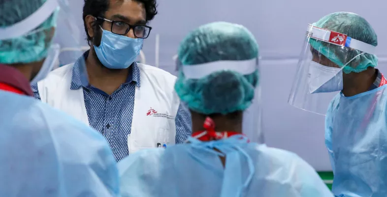 Vier Ärzte beraten sich. Sie sind komplett in Schutzkleidung gehüllt.