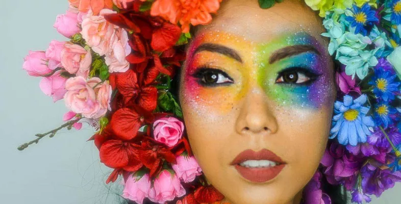 Frau mit regenbogenfarbenem Blumenkranz und Augenmakeup.