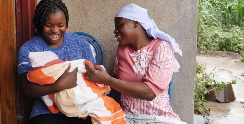 Zwei Frauen sitzen auf einer Bank. Eine hält ein Baby im Arm.