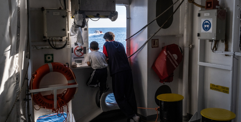 Zwei Jungen stehen am Fenster eines Schiffes und schauen auf das Meer.