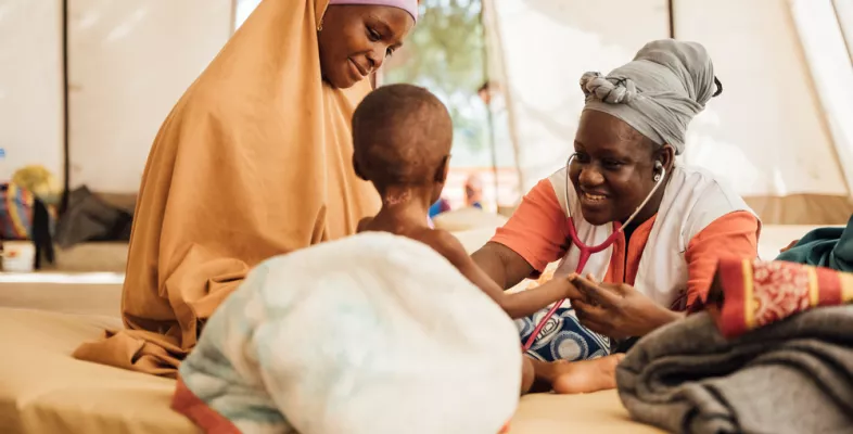 Unsere Ärztin Faïza Ouedraogo hat den zweijährigen Edriss während ihrem Einsatz in Niger behandelt. Spenden: Ärztin hört Kleinkind mit Stethoskop ab, daneben Mutter