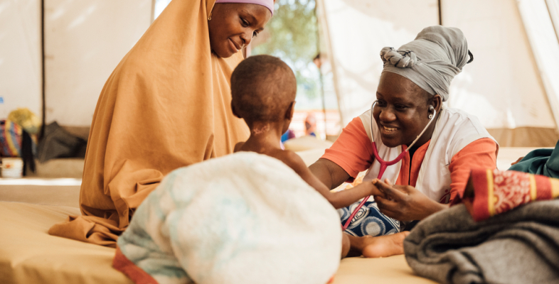 Unsere Ärztin Faïza Ouedraogo hat den zweijährigen Edriss während ihrem Einsatz in Niger behandelt. Spenden: Ärztin hört Kleinkind mit Stethoskop ab, daneben Mutter