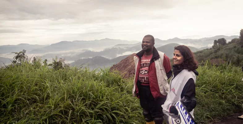Unsere Finanzkoordinatorin Flavia und unser Fahrer Japhet warten nach einer Panne auf dem Weg nach Miandja, D.R. Kongo, auf die Weiterfahrt. Finanzkoordinator*in und Fahrer Panne in gebirgiger Landschaft