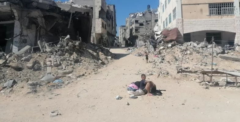 Junge sitzt auf Sandstraße in zerstörter Stadt