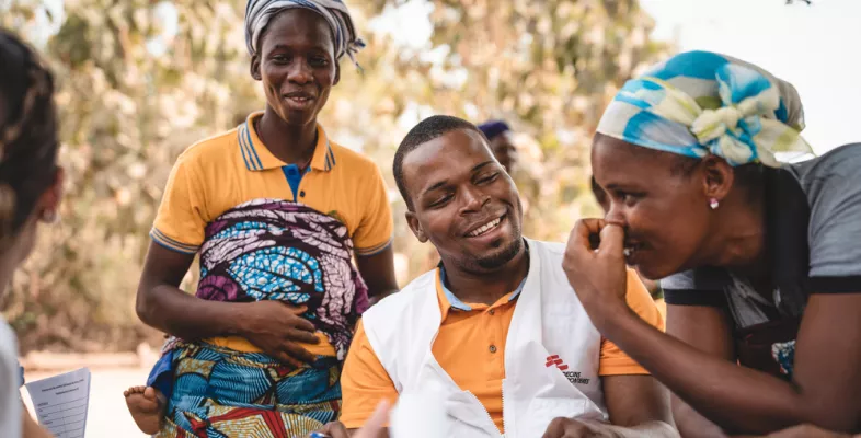 Mitarbeiter in Benin, sitzend im Gespräch mit zwei Frauen