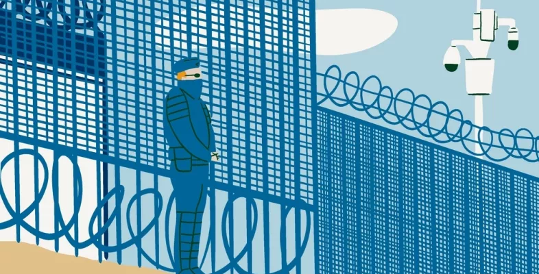 Uniformierter Mann steht vor einem Stacheldrahtzaun