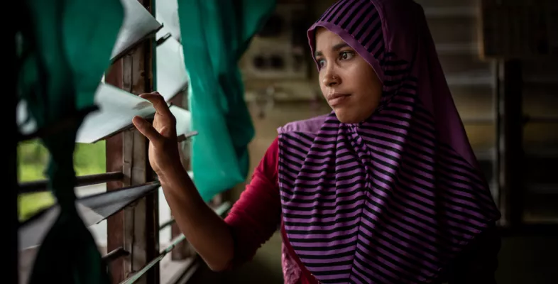 Die gefährliche Fluchtroute vieler Rohingya endet in Malaysia. Eine Frau sitzt im Dunkeln und blickt durch vergitterte Fenster